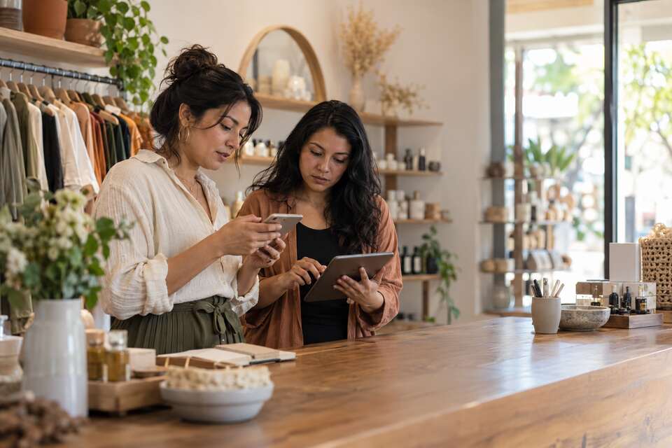 Dos personas del equipo de una tienda revisando una tableta y un móvil.
